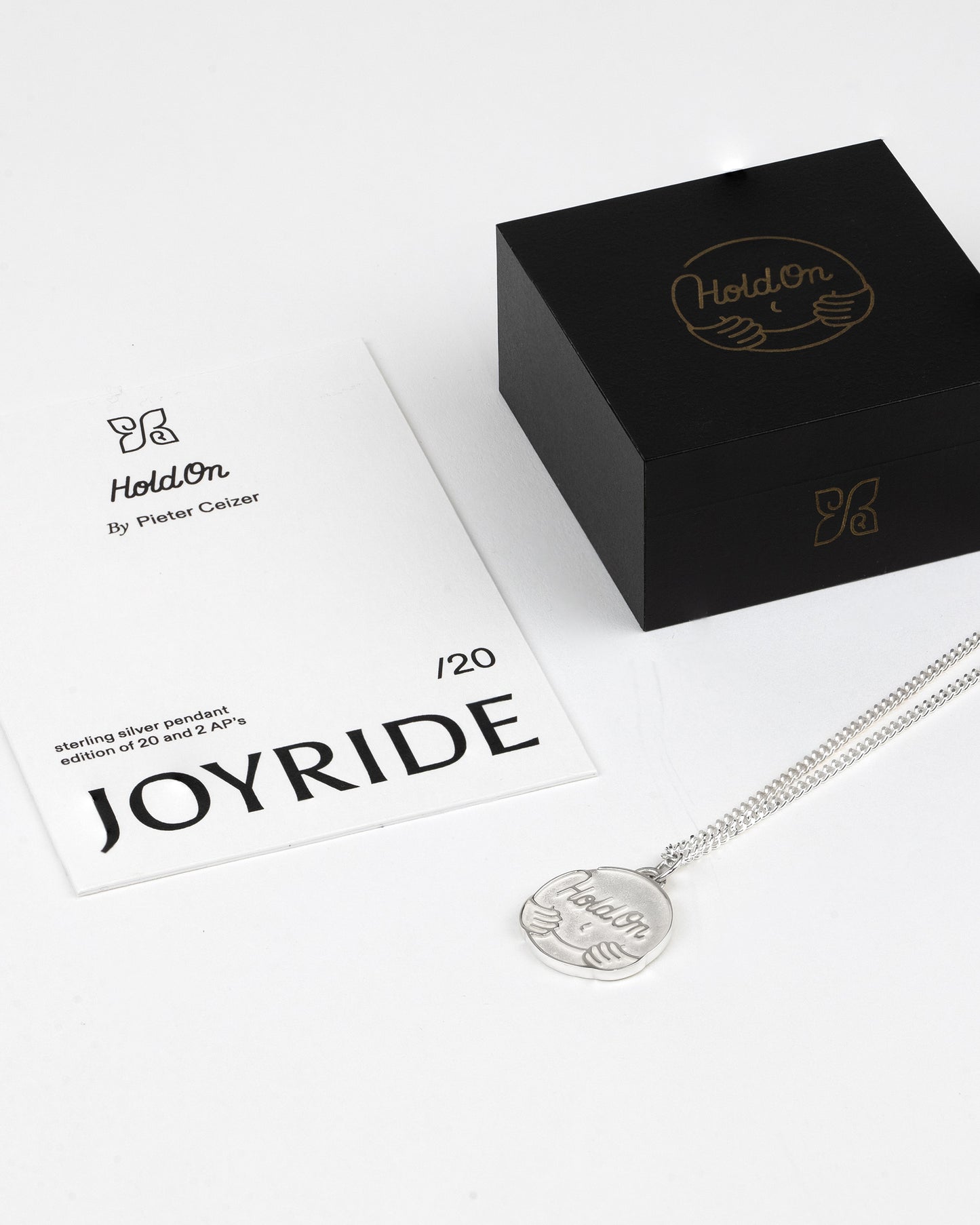 Silver necklace with pendant on a white background, featuring 'Hold On' branding. BY PIETER CEIZER