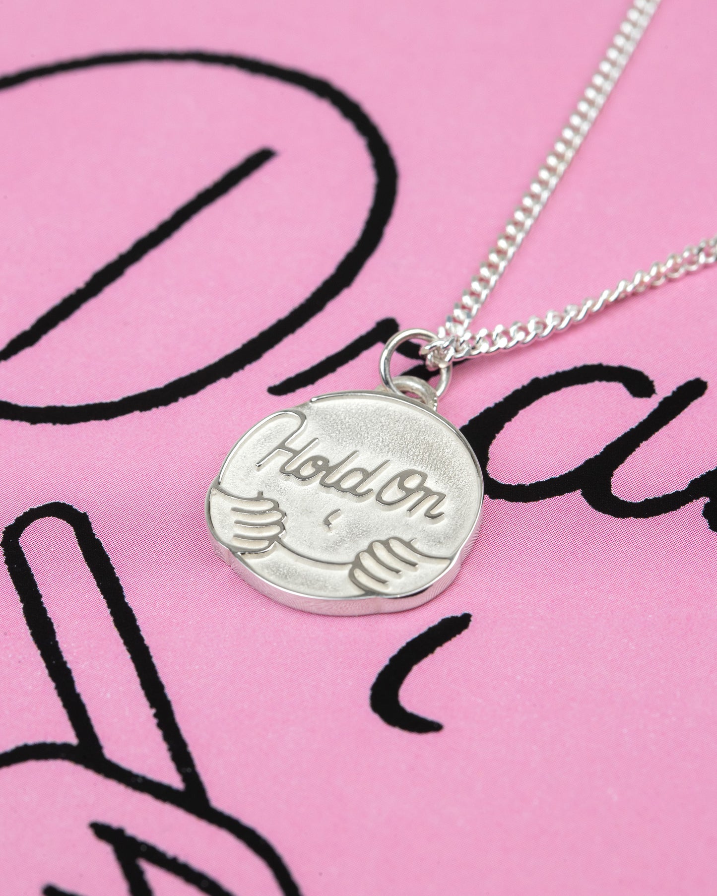 Silver necklace with a pendant on a pink background with black text BY ARTIST PIETER CEIZER
