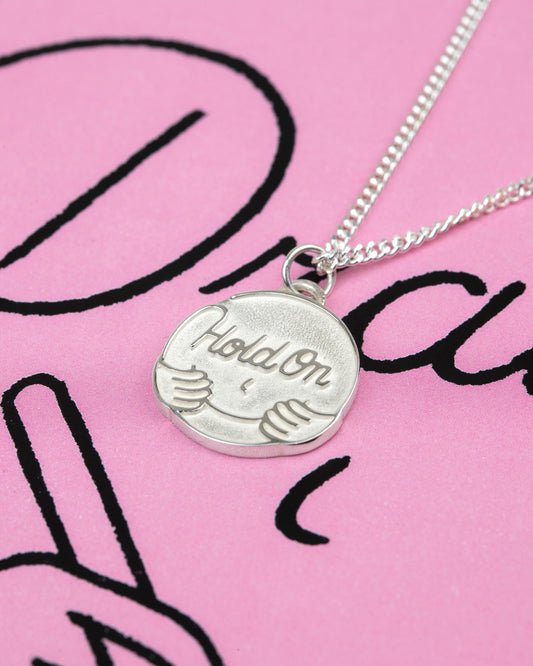 Silver necklace with a pendant on a pink background with black text BY ARTIST PIETER CEIZER
